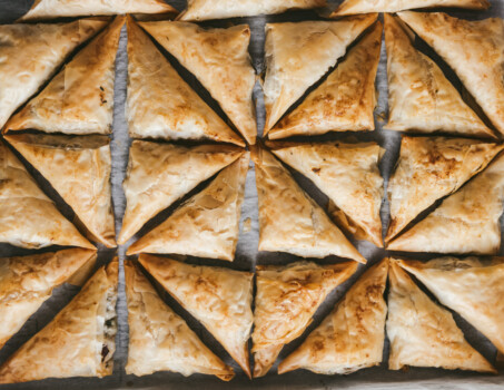 Top view of geometrically placed baked spanikopita triangles on parchment paper
